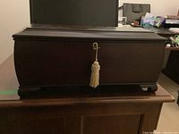 Front view of the rectangular wood footed storage box with the decorative tassel-key in lock.