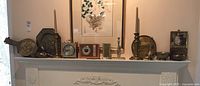 Wide shot of mantel displaying brass duck, candle sticks, wall plates, clocks, snake figure, and mail wall hanger.