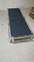 Full view of cot opened, showing navy blue fabric surface and tubular chrome frame on carpeted floor