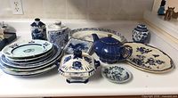 Wide view of the lot showing assorted blue and white ceramic plates, ginger jars, a teapot, and egg holders arranged on a counter