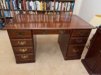 Front view of wood desk showing 4 drawers on each side and central knee space under polished top.