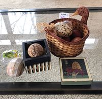 Woven duck basket with assorted decorative eggs made of wood, glass, and agate placed on a glass table.