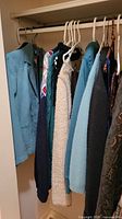 Photo showing seven garments hanging on hangers. Includes jackets, sweaters, and blouses in blue, cream, peach, and patterned materials.