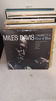 Front view of approximately 35 LP records stacked vertically showing mostly the spines. "Miles Davis Kind of Blue" is frontmost album visible.