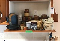Shelf with a collection of pottery items including multiple jugs, mugs, a bowl, and fish wall hanging.
