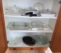 Full view inside cabinet showing the glass bakeware including casseroles, pie plates, divided dish, and handles.