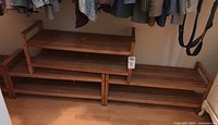 Four wooden slat shoe racks stacked in two layers within a closet space, each rack showing slatted wood surfaces and side frames.