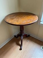 Round wooden parlor table positioned in corner, showing round top surface with noticeable wear and wood grain.