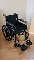 Front-left angled view of the black foldable manual wheelchair showing seat, armrests, and footrests
