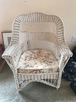Front view of the white wicker chair showing woven design and floral seat cushion.
