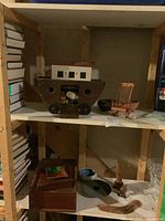 Wooden Noah's Ark with small house on top, positioned on a wooden shelf with other wooden items including a rocking chair and rectangular box