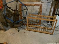 Overall view showing a vintage wooden yarn spinning machine next to two wooden drying racks on a concrete floor in a basement.