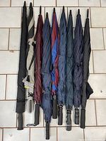 Nine closed umbrellas side by side showing variety of handles and canopy fabrics