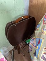 Stack of four dark brown wooden folding tray tables in folded position