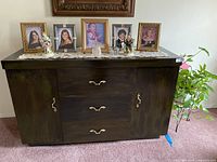 Photo showing the closed black wooden cabinet with decorative items on top including framed photos and figurines.