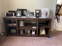 Front view of dark wood display stand with photo frames on the top and inside compartments, showing six storage sections with adjustable shelves.