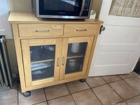 Light wood kitchen cabinet with glass panel double doors and two upper drawers, microwave on top for scale