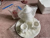 Photo showing all silver plated items wrapped in plastic, including a round tray and three holders, on carpet.