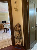 Corner corner shelf with bronze metal frame holding decorative teapot and figurines, placed in a room corner