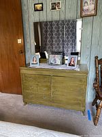 Front view of vintage green wooden dresser with six drawers and attached mirror, with framed photos on top.