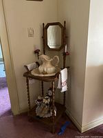 Full view of the wooden washstand with a porcelain wash basin on top, porcelain doll seated on a lower shelf, mirror and candle holders visible, towels hanging on the sides.