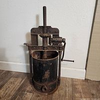 Front view of the vintage cast iron cider press showing cylindrical chamber and spout, heavy rust present