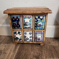 Front view of wooden spice rack showing six ceramic drawers with colorful decorative patterns.