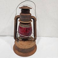 Front view of rusted Dietz Little Wizard red globe lantern with wire handle and base visible