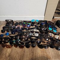 Wide view of the entire collection of sunglasses laid out on the floor, showing various frame and lens colors.