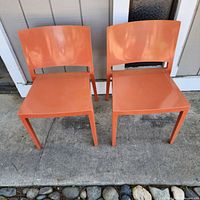 Front view of two orange Kartell Lizz stacking chairs side by side on a concrete surface.
