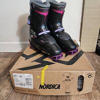 Front angled view of Nordica AFX snow boots on top of original box showing black and purple color with size details on box