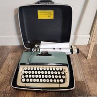 Smith Corona Galaxie II manual typewriter seated in its original hard case with a sheet of paper loaded, showing the full front and keyboard.