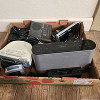 Overview of six electronic devices including Sony alarm clocks and audio dock in a cardboard box