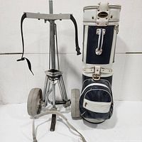 Golf bag and metal caddy displayed upright, showing full view of bag, caddy handle, straps and wheels.