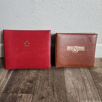 Two stamp collection albums side by side on floor: red album with gold stars and brown album titled 'Birds & Flowers of the 50 States'