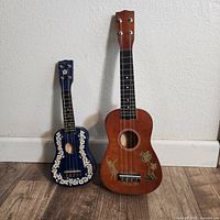 Photo showing two Hawaiian ukuleles, one brown with decorative dancer and palm trees, one blue with floral print.