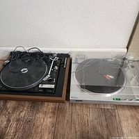 Two turntables side by side on the floor, a wooden framed Dual 1237 on the left and a silver Sony PS-LX5 with dust cover on the right.