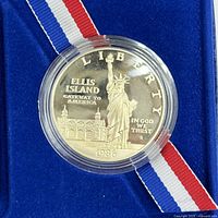 Close-up of front side of the 1986 Liberty Silver Dollar coin showing Statue of Liberty and Ellis Island text.