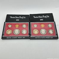 Two 1982 United States proof coin sets displayed side by side in original black packaging with red backing.