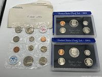 Two 1983 US Proof Sets in blue packaging and one mixed set of uncirculated coins in plastic with labels, displayed on white background.