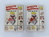 Two Dennis the Menace pocket books side by side showing full front covers with tricycle illustration and character headshots.