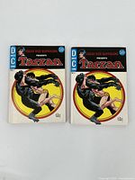 Photo showing two Tarzan comic digest books, both DC Comics issue number 1 with identical cover art of Tarzan fighting a panther against a yellow and red circular background.