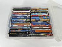 Top view of the Blu-ray DVDs stacked neatly inside a transparent plastic storage container. Titles include Disney and Pixar animated films, classic family movies, and cartoon collections.