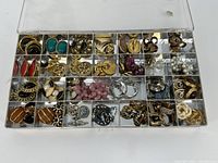 View of the full clear plastic organizer box with all compartments filled with various costume jewelry pieces such as earrings, brooches, and bracelets.