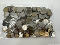 Large clear plastic bag filled with an assortment of various coins of different sizes and metallic colors.