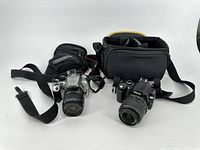 Lot with Canon EOS camera and Nikon D40 camera, each with carrying bags and shoulder straps shown side by side.