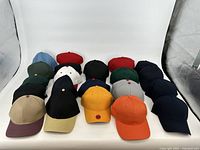 Photo of 21 plain baseball caps in various colors arranged on a white surface showing front view of caps
