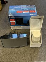 Photo showing Coby speaker system with original box, glossy black speaker, and white smart speaker in box.
