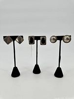 Photo of all three pairs of sterling silver earrings on black stands: diamond shaped, rectangular with black inlay, round dome with rope edges.