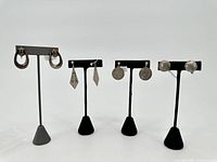 Four pairs of sterling silver earrings displayed on black and grey stands, showing variety of shapes and patterns.